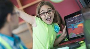 A child excitedly holding a laptop displaying the video game "Minecraft"