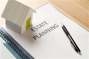 Photo shows a paper saying the words "Estate Planning" with a pen resting on the paper