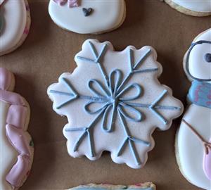 A snowflake cookie is shown laying on a table, decorated with blue lines of icing.