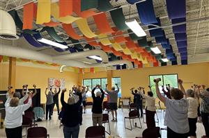Bone Builder participants are shown stretching their arms up while holding weights and maintaining their balance