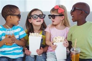 Children smile at each other while eating popcorn and watching a movie