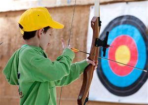 A child holding a bow and arrow getting ready to aim at a target.