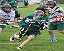 3 boys lacrosse players- 1 with ball cradling, other two chasing